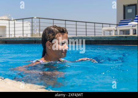 Orientalisches Aussehen lächelndes weibliches Kind posiert in ruhigem blauem Wasser. Stockfoto