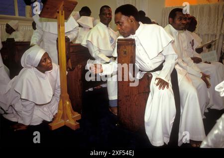 Männer Frauen segregiert, schwarze britische Kirche Leben 1990s UK. Die Bruderschaft des Kreuzes und des Sterns, die Mitglieder der Kirche, sind auf einen Ausflug und Kreuzzug von London nach Manchester gegangen, um den 19. Jahrestag der Kirche in Großbritannien zu feiern. Bei dem Abendgebetsgottesdienst werden Frauen und Männer getrennt voneinander innerhalb der Kirche getrennt. Frauen müssen auf Hände und Knie gehen, um mit männlichen Ältesten der Kirche zu reden, wenn sie gerufen werden. Moss Side, Manchester, England 1993 HOMER SYKES Stockfoto