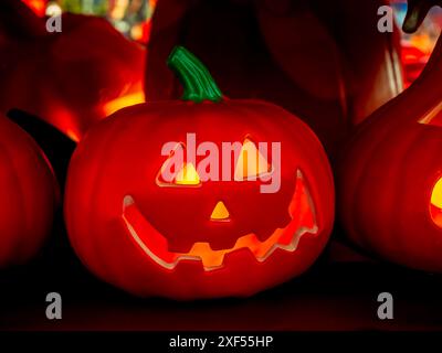 Nahaufnahme des roten Halloween Jack o Lantern Kürbis mit gruselig lächelndem Gesicht. Oranger Kürbiskopf lächelndes Gesicht mit offenem Mund, glühend auf dunklem Ba Stockfoto