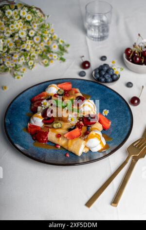 Köstliche Crepes mit Sommerbeeren und Toppings, gerollte dünne Pancakes mit Hüttenkäse Füllung auf einem Teller Stockfoto
