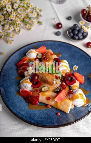 Köstliche Crepes mit Sommerbeeren und Toppings, gerollte dünne Pancakes mit Hüttenkäse Füllung auf einem Teller Stockfoto
