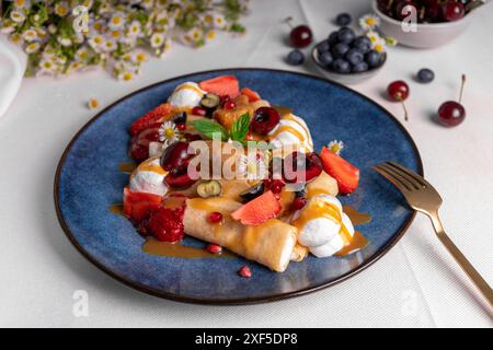 Köstliche Crepes mit Sommerbeeren und Toppings, gerollte dünne Pancakes mit Hüttenkäse Füllung auf einem Teller Stockfoto