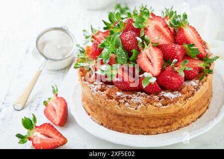 Erdbeerkuchen. Hausgemachter und köstlicher Erdbeer-Biskuitkuchen mit frischen Sommerfrüchten, Frischkäsezuckerguss und Zuckerpulver auf weißem Marmor Stockfoto