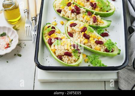 Zucchini gefüllt mit Petitim, roten Bohnen, Mais mit Basilikum und Soße, gebacken auf einem alten, zerrissenen Fliesenhintergrund. Draufsicht. Stockfoto