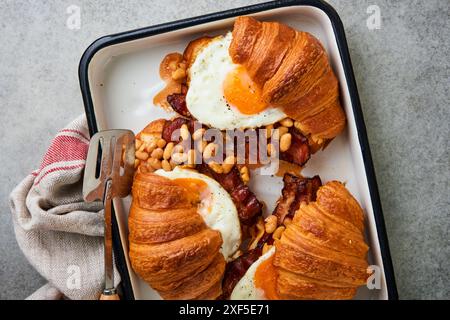 Croissants, englisches Frühstück. Köstliches frisches Frühstück gegrillt drei Croissants mit Speck, Spiegeleiern und Bohnen in Tomatensauce und zwei Gläsern C. Stockfoto