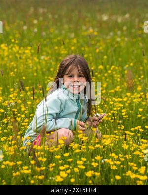 Ein niedliches kleines Mädchen spaziert auf einer Landstraße und pflückt Wildblumen und Löwenzahn auf einer Blumenwiese. Sommersaison. Aktivitäten im Freien für Kinder. Stockfoto