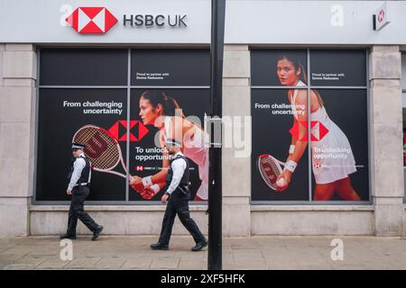 Wimbledon, London, Großbritannien 1. Juli 2024. Polizeibeamte gehen an einer lokalen Filiale der HSBC Bank im Stadtzentrum von Wimbledon vorbei. Mit einem Bild der britischen Tennisspielerin Emma Raducanu als globale Markenbotschafterin. Quelle: Amer Ghazzal/Alamy Live News Stockfoto