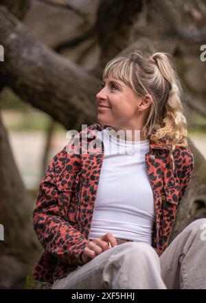 Glückliches weißes Mädchen sitzt im Park zwischen den Bäumen und genießt das Leben und atmet frische Luft. Porträt eines Mädchens, das wegschaut Stockfoto