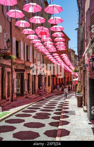 Schwebende pinkfarbene Regenschirme, die über der Rue Amiral de Grasse in der Altstadt von Grasse an der französischen Riviera, Côte d'Azur, Provence, Frankreich aufgehängt werden Stockfoto