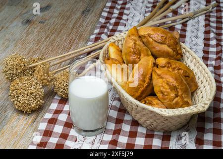 Torten mit Füllung in einen Korb auf einem Holzbrett, daneben gibt es ein Glas Milch und getrocknete Pflanzen. Rustikales Motiv, Draufsicht und Kopierraum. Pirozh Stockfoto