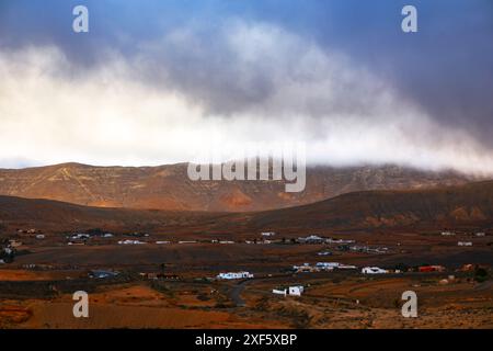 Bewölkter Himmel hängt über einer Wüstenlandschaft auf den Kanarischen Inseln Fuerteventura. Die Landschaft ist karg und einsam, ohne Lebenszeichen. Die Szene ist düster Stockfoto