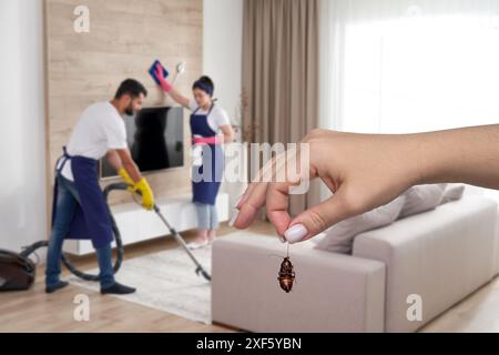 Weibliche Hand, die tote Kakerlake mit Reinigungskräften im Hintergrund hält. Konzept der Schädlingsbekämpfung und professionellen Reinigung im Haushalt Stockfoto