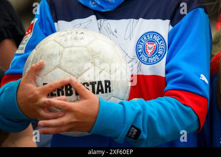 Gettorf, Deutschland. Juli 2024. Fußball: Bundesliga, Holstein Kiel Training Kick-off. Ein junger Fan trägt ein signiertes Fußballtrikot und wartet auf dem Sportplatz Gettorfer SC mit einem Ball in der Hand auf die holsteinischen Kieler Spieler. Quelle: Gregor Fischer/dpa/Alamy Live News Stockfoto