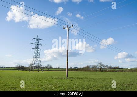 Nationaler Netzstrompylon und Strommast in Großbritannien, auf grünem Feld vor blauem Himmel mit Wolken Stockfoto