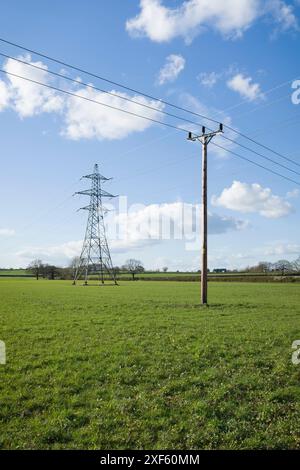 Nationaler Netzstrompylon und Strommast in Großbritannien, auf grünem Feld vor blauem Himmel mit Wolken Stockfoto