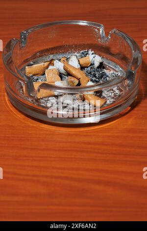 Vertikales Foto des Glasaschenbechers mit Zigarettenkippen auf dem Tisch und Negativraum Stockfoto
