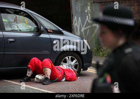 Manchester, England, Großbritannien. Juli 2024. Ein Polizist steht, der einen abgesperrten Bereich um Aktivisten schützt, die an einem Auto festgehalten sind und den Zugang zu den Büros der CDW blockiert. Die Palästinensische Aktion richtet sich direkt an Unternehmen von Elbit Systems, aber auch Aktivisten haben Partnerunternehmen des israelischen Rüstungsunternehmens und diejenigen, die in das Unternehmen investieren, ins Visier genommen. Fünf Unternehmen haben im letzten Jahr alle Beziehungen zum Waffenhersteller abgebrochen, nachdem sie wiederholte direkte Aktionen erlitten hatten, einschließlich der Schließung von Büros durch die Palästinensische Aktion. CDW bietet IT-Lösungen für Elbi Stockfoto