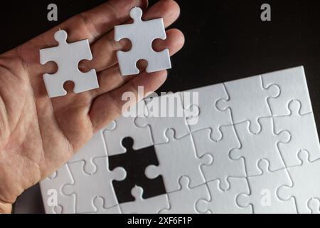 Eine Hand, die zwei weiße Puzzleteile hält, wobei eines fehlt. Konzept der Vollendung und Zufriedenheit, da das fehlende Stück der Schlüssel zum Abschluss des Puzz ist Stockfoto