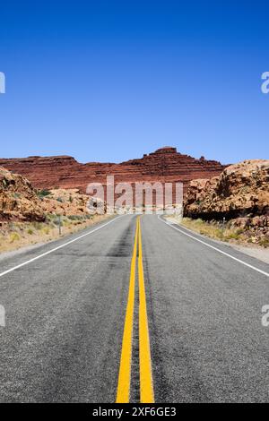 Zweispurige Straße mit doppelter gelber Linie, die durch die Landschaft im Süden Utahs führt und sich roten Felsen nähert Stockfoto