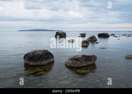 Eine ruhige Meereslandschaft mit großen Felsen im Vordergrund und einer Insel in der Ferne unter einem bewölkten Himmel im Awenda Provincial Park, Ontario Kanada Stockfoto