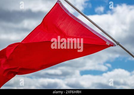 Rote Warnflagge, die im Wind gegen blauen Himmel fliegt Stockfoto