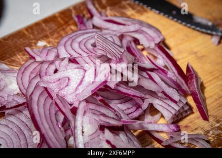 Scheiben von roten Zwiebeln, die zu den Chilis hinzugefügt werden. Stockfoto