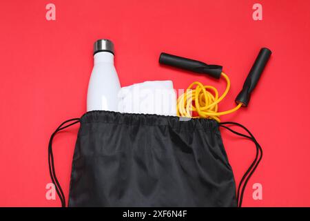 Schwarze Tasche mit Kordelzug, Thermoflasche und Überspringseil auf rotem Hintergrund, flacher Lay Stockfoto