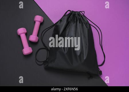 Schwarze Tasche mit Kordelzug und Kurzhanteln auf farbigem Hintergrund, flacher Lay Stockfoto