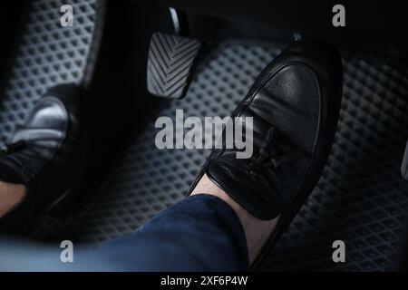 Mann in schwarzen Schuhen, der auf das Pedal der Autobremse drückt, Nahaufnahme Stockfoto