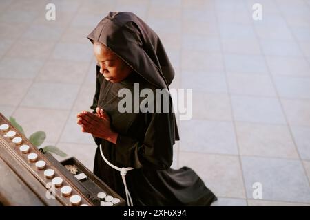 Hochwinkelansicht der jungen afroamerikanischen Nonne, die auf ihren Knien steht und vor dem Altar in der katholischen Kirche betet Stockfoto