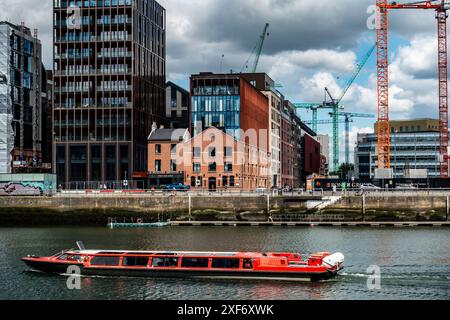 Das leuchtend rote, mit Glasdach versehene Ausflugsboot „Spirit of Docklands“, das am North Wall Quay auf dem Fluss Liffey, Dublin, Irland, vorbeifährt. Stockfoto