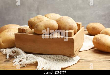 Viele frische Kartoffeln in Kiste auf Holztisch, Nahaufnahme Stockfoto