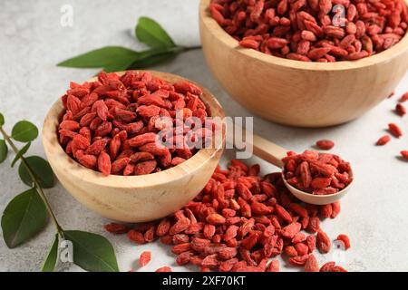 Getrocknete Goji-Beeren, Schüssel und grüne Blätter auf einem hellen, strukturierten Tisch, Nahaufnahme Stockfoto