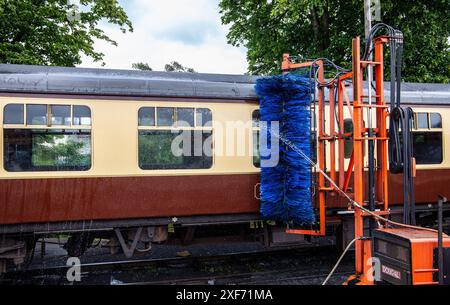 Alte, alte Personenzugwagen, die einer automatischen Reinigung unterzogen werden, mit blauen Bürsten, die ihre Seiten an einem Bahnhof reinigen Stockfoto