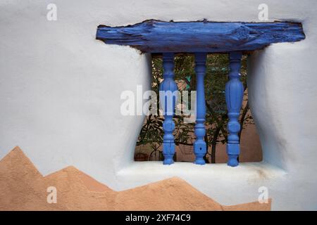 Nordamerika, Usa, New Mexico, Albuquerque. Blauer Holzsturz und geschnitzte Spindeln unterstützen eine dekorative Fensteröffnung in einer Stuckwand. Stockfoto