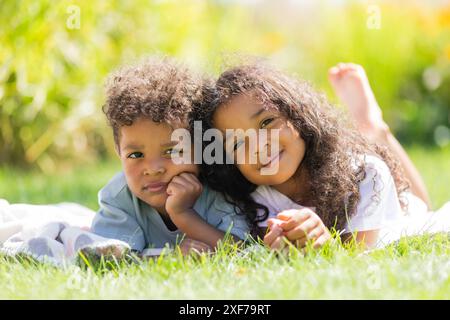 Zwei kleine afroamerikanische Kinder, ein Junge und ein Mädchen, liegen im Sommer auf dem grünen Gras Stockfoto