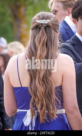 Eine junge Frau mit langen welligen Haaren, die ein blaues Kleid mit einer dekorativen Haarspange auf einem Ballfest im Freien in Ludvika, Schweden, trägt. Vertikale Aufnahme. Stockfoto