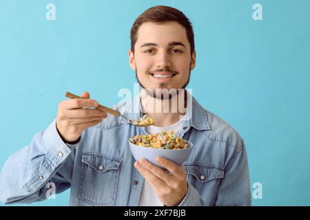 Schöner junger Mann, der leckere Müsliringe auf blauem Hintergrund isst Stockfoto