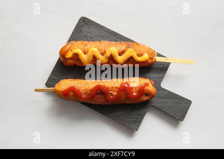 Schwarzes Brett mit leckeren Maishunden mit Ketchup und Senf auf grauem Hintergrund Stockfoto