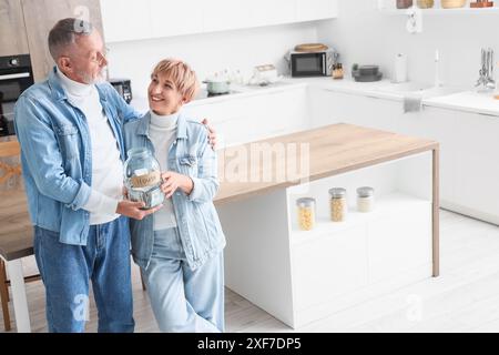 Ein reifes Paar hält ein Glas mit Geld für das Haus in der Küche Stockfoto