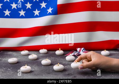 Weibliche Hand mit brennenden Kerzen und Windrad auf dem Tisch vor der Flagge der USA. Nationalfeiertag des Gebets und des Gedenkens für die Opfer des Terroristen AT Stockfoto