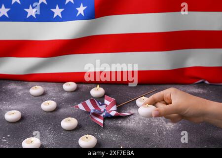 Weibliche Hand mit brennenden Kerzen und Windrad auf dem Tisch vor der Flagge der USA. Nationalfeiertag des Gebets und des Gedenkens für die Opfer des Terroristen AT Stockfoto