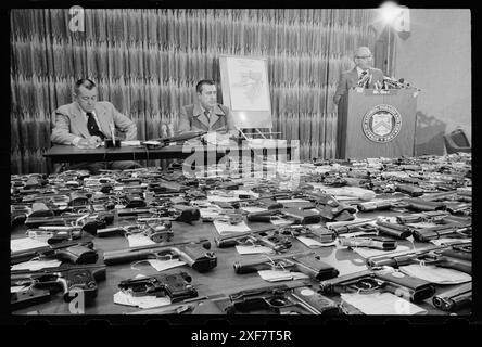 Nicht identifizierte ATF-Beamte sitzen an einem Tisch, während ein anderer an einem Rednerpult hinter einer Ausstellung konfiszierter Handfeuerwaffen im Bureau of Alcohol, Tobacco and Firearms, Washington, District of Columbia, spricht. 1976. (Foto: Thomas O'Halloran/U S News and World Report Collection) Stockfoto