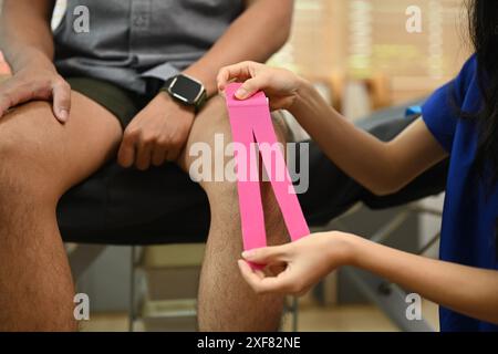 Eine Physiotherapeutin, die pinkfarbene kinesio-Klebeband am Knie des Patienten anbringt. Physiotherapie und Rehabilitationskonzept Stockfoto