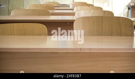 Foto eines leeren Klassenzimmers mit Holzschreibtischen und -Stühlen in Reihen, Sonnenlicht strömt durch die Fenster. Stockfoto