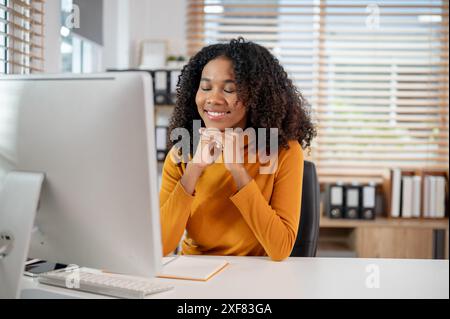 Eine traumhafte, glückliche schwarze Geschäftsfrau sitzt mit geschlossenen Augen an ihrem Schreibtisch im Büro und träumt von ihrem Karriereerfolg. Stockfoto