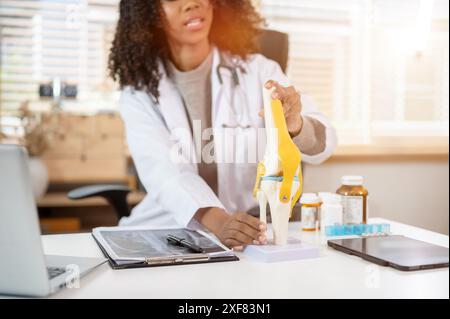 Nahaufnahme eines professionellen Schwarzen Orthopäden, der einem Patienten während einer ärztlichen Beratung im Clini ein Kniegelenkmodell erklärt und zeigt Stockfoto