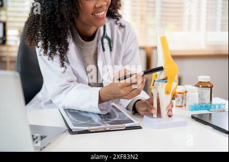 Nahaufnahme eines professionellen Schwarzen Orthopäden, der einem Patienten während einer ärztlichen Beratung im Clini ein Kniegelenkmodell erklärt und zeigt Stockfoto