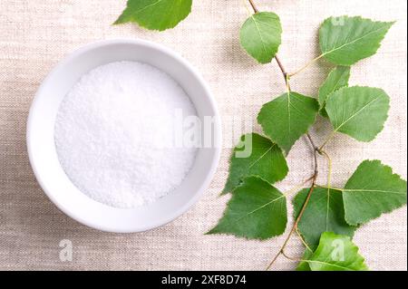 Birkenzucker, Tafelsüß auf Xylit-Basis, in einer weißen Schüssel auf Leinengewebe. Auch Xylit genannt, ein Zuckerersatz natürlichen Ursprungs. Stockfoto