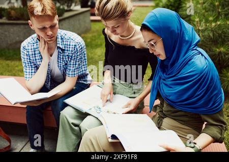 Multikulturelle Freunde diskutieren Studienarbeit, arbeiten an Projekten, machen gemeinsame Hausaufgaben draußen auf dem Campus. Kaukasische und muslimische Studenten Stockfoto